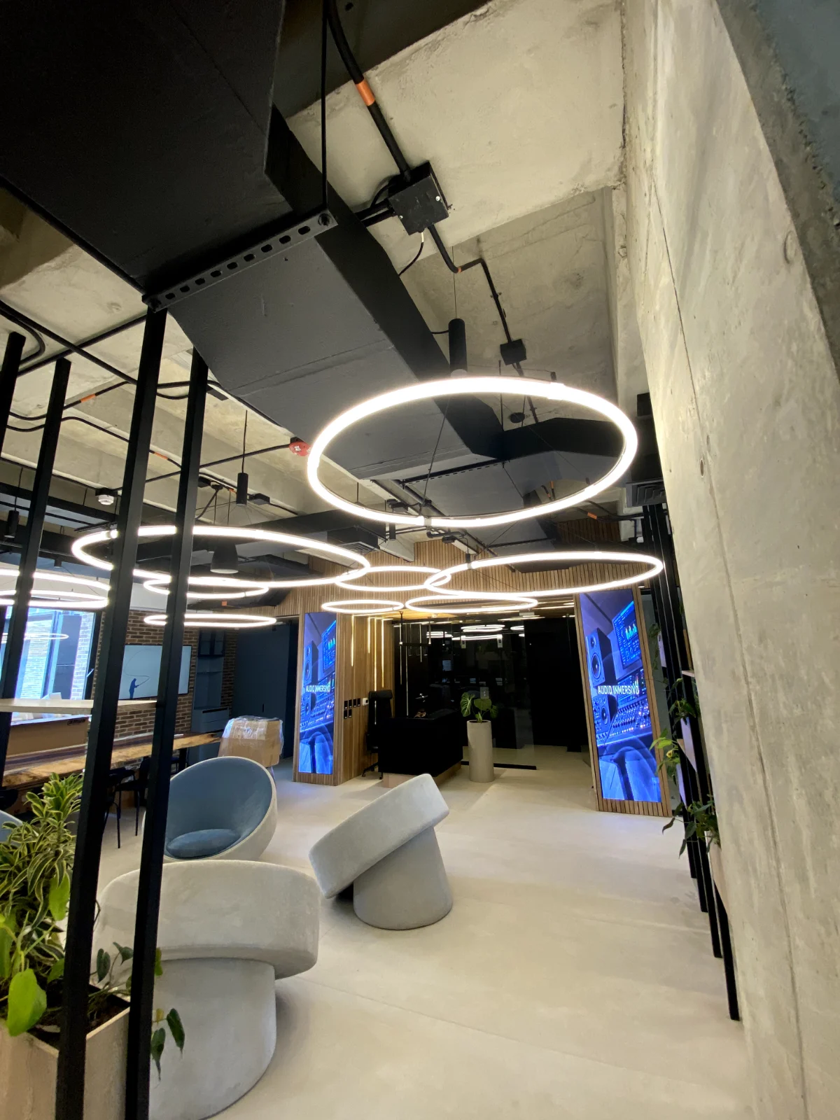 Lobby de oficinas con ducto de aire acondicionado negro, rejillas en el techo y lámparas circulares